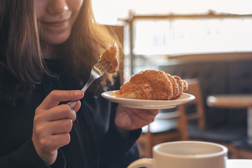 Closeup image of an asian woman holding and eating a piece of croissant for breakfast in the morning