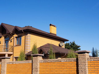 Big brick home with chimney, rain gutter and brick fence under blue sky, side view