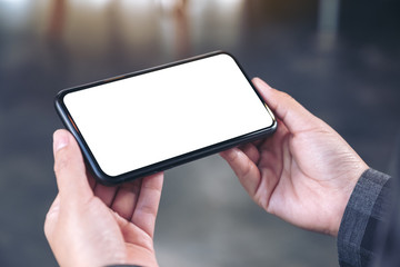 Mockup image of hands holding black mobile phone with blank white screen  horizontally