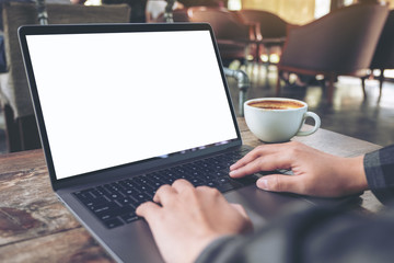 Mockup image of hands using and typing on laptop with blank white desktop screen with coffee cup on wooden table in cafe