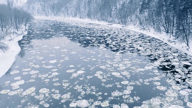 Winter river ice floe drifting, snow falling, aerial view