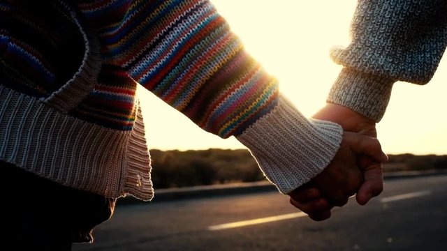 Adult mature couple waling holding hands with love and romance on a street with sunset in backlight and background - forever together concept for people enjoy life and romantic light