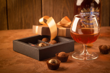 A glass of strong alcoholic drink brandy or brandy and a box of chocolates on a dark background.