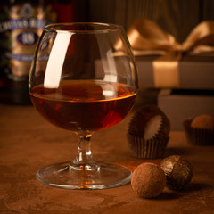 A glass of strong alcoholic drink brandy or brandy and a box of chocolates on a dark background. Selective focus.
