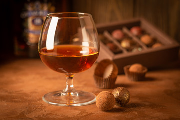 A glass of strong alcoholic drink brandy or brandy and a box of chocolates on a dark background. Selective focus.