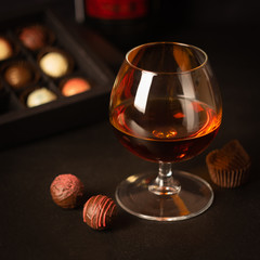 A glass of strong alcoholic drink brandy or brandy and candy made of Belgian chocolate on a dark background.