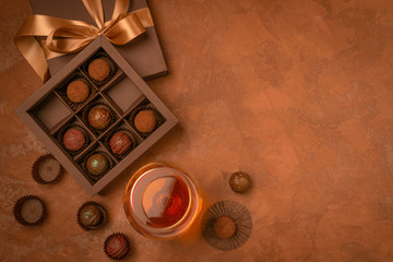 A glass of strong alcoholic drink brandy or brandy and a box of chocolates on a dark background. Flat layout.