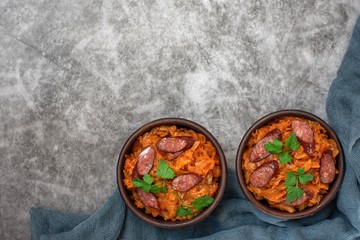 Cabbage stew in bowl with smoked sausages on grey background. Top view, with copy space