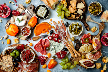 Appetizers table with antipasti snacks. Brushetta or authentic traditional spanish tapas set, cheese and meat platter over grey concrete background. Top view