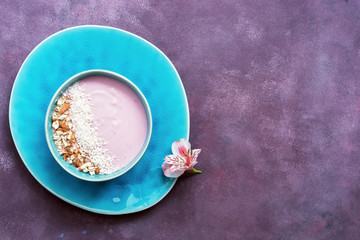 Obraz na płótnie Canvas Fresh pink yogurt with nuts and coconut flakes in beautiful blue dishes on a purple background. Top view, place for test.