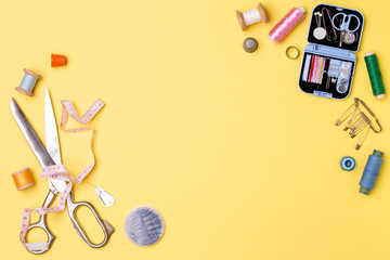 Composition with threads and sewing accessories - scissors, centimeter, pins on yellow background.