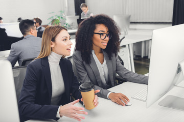 smiling young multiethnic businesswomen using desktop computer together in office