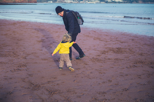 Toddler playing with grandfather on beach