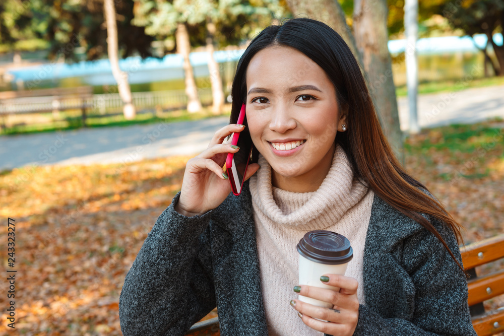 Sticker smiling young asian woman wearing coat sitting on a bench