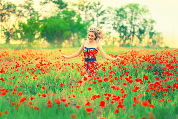 Obraz na płótnie Canvas cheerful attractive pretty girl with blond curly flying hair runs across the poppy field and laughs, the wind blows in her face, dressed in a short cute red dress with bare shoulders open