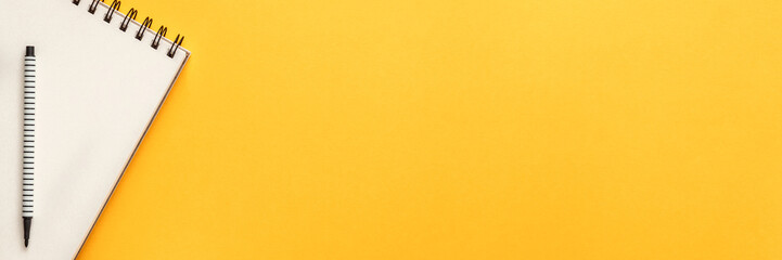 Blank yellow background with place for text. Copy space. Sketchbook and felt-tip pen as a decoration. Panoramic view from above. Flat lay, real photo. Minimal composition