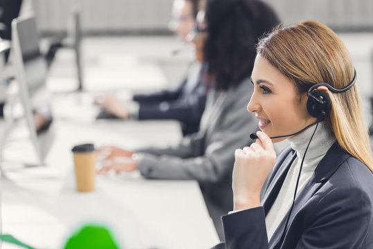 side view of smiling young businesswoman in headset working with colleagues in office