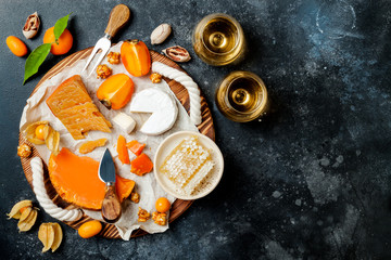 Obraz na płótnie Canvas Cheese variety board or platter with cheese assortment, persimmons, honey and nuts. Black stone background. Top view, flat lay
