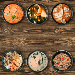 Tasty Asian dishes in black bowls. Wooden brown background with copy space.