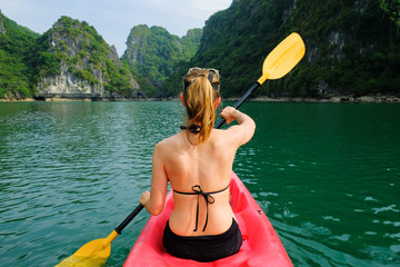 Woman on kayak paddling through karst islands and dense jungle in Halong Bay / Cat Ba island areas...