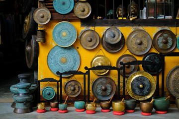 A colorful collection of ornamental gongs, sound bowls and buddha statues hanging on a yellow wall in a shop front in Hoi An, Vietnam.
