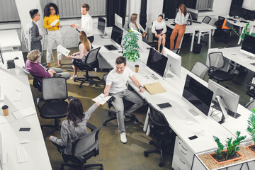 high angle view of professional young colleagues working with papers and computers in open space office