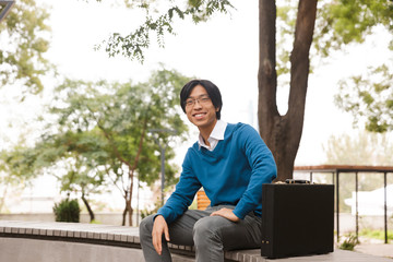 Smiling young asian business man sitting outdoors