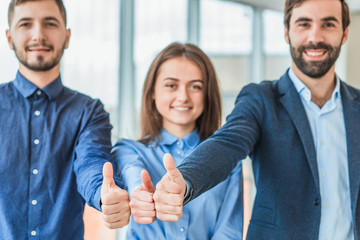 Three young serious partners in the office. During this, they are standing on the gesture of the class on their elongated hands.