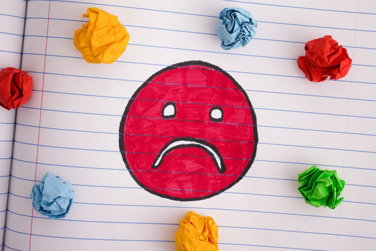 Sad face with colorful crumpled paper balls on notebook sheet