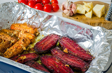 A healthy food. Spiced beets and carrots lay in a cooking form next to tomatoes, parmesan, garlic and cheese grater