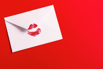 Red lipstick kiss on white envelope on red. Valentine's day background. Love letter concept.