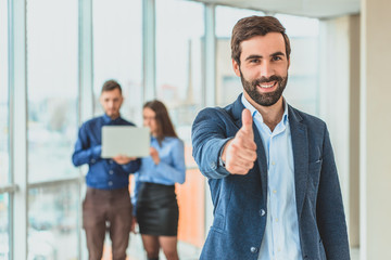 Fototapeta premium A businessman stands in the office showing a hand gesture of a class. During this time, he stands against the background