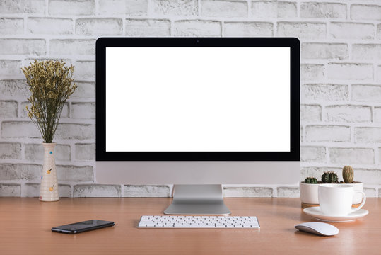 Blank screen of all in one computer with dry flowers, smart phone, coffee cup and cactus vase on white bricks background
