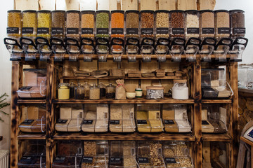 Front view of variety of seeds and nuts displayed in grocery store. Zero waste shopping - shelf with glass jars full of dry food in organic shop.