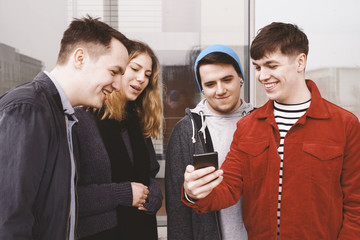 young man showing something funny on his smart phone to a group of friends - urban teenagers having fun and laughing together