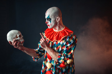 Mad bloody clown holds human skull in red wig