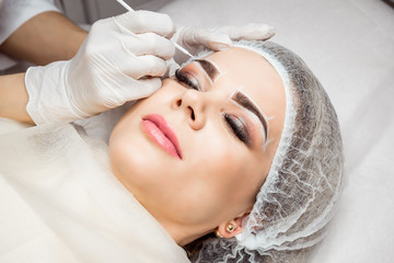 Obraz na płótnie Canvas Permanent Makeup For Eyebrows. Closeup Of Beautiful Woman With Thick Brows In Beauty Salon. Beautician Doing Eyebrow Tattooing For Female Face. Beauty Procedure.