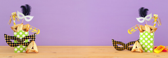 Purim celebration concept (jewish carnival holiday) over wooden table and purple background.