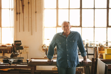 Senior man standing by a table in his carpentry workshop - obrazy, fototapety, plakaty