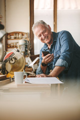 Senior carpenter at his workshop using mobile phone