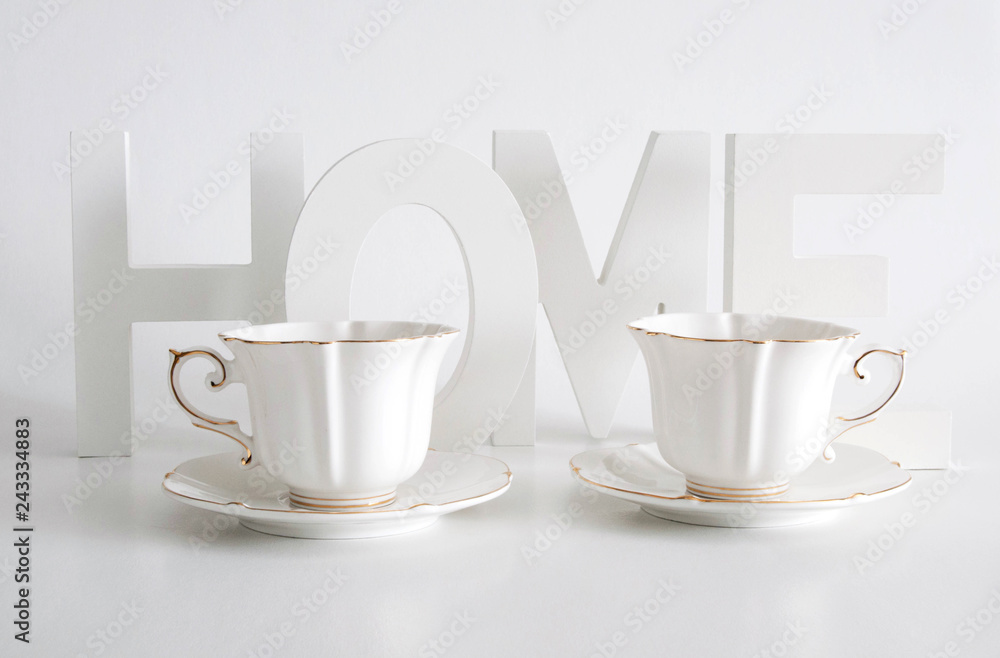 Sticker white letters, word home and two elegant white cups on white background. home decor