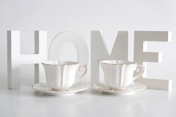 White letters, word home and two elegant white cups on white background. Home decor