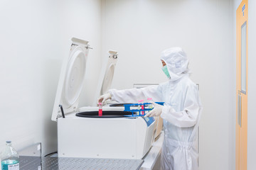 A scientist in sterile coverall gown placing cell culture flasks in the CO2 incubator. , Cleanroom...