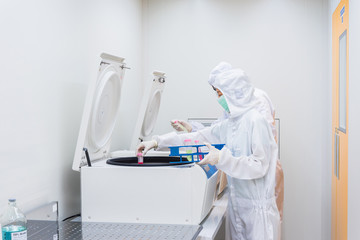 A scientist in sterile coverall gown placing cell culture flasks in the CO2 incubator. , Cleanroom...