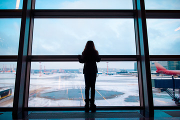 Fototapeta na wymiar Little girl in airport near big window while wait for boarding