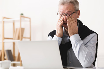 Hard day. Elderly man feeling tired, working on laptop