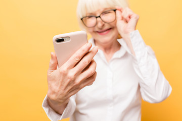 Phone conversation. Positive aged woman smiling while talking on the phone isolated over yellow background.