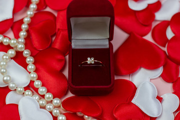 Ring in a red box and pearls on a background of hearts of red and white. Wedding ring in the box. Marriage proposal concept, Valentine's Day, International Women's Day.