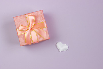 A gift in a beautiful box and a white heart on a pink background. Valentine's Day, International Women's Day.