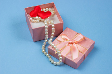 pink gift box with pearls and hearts on a blue background. The concept of the holiday Valentine's Day, International Women's Day